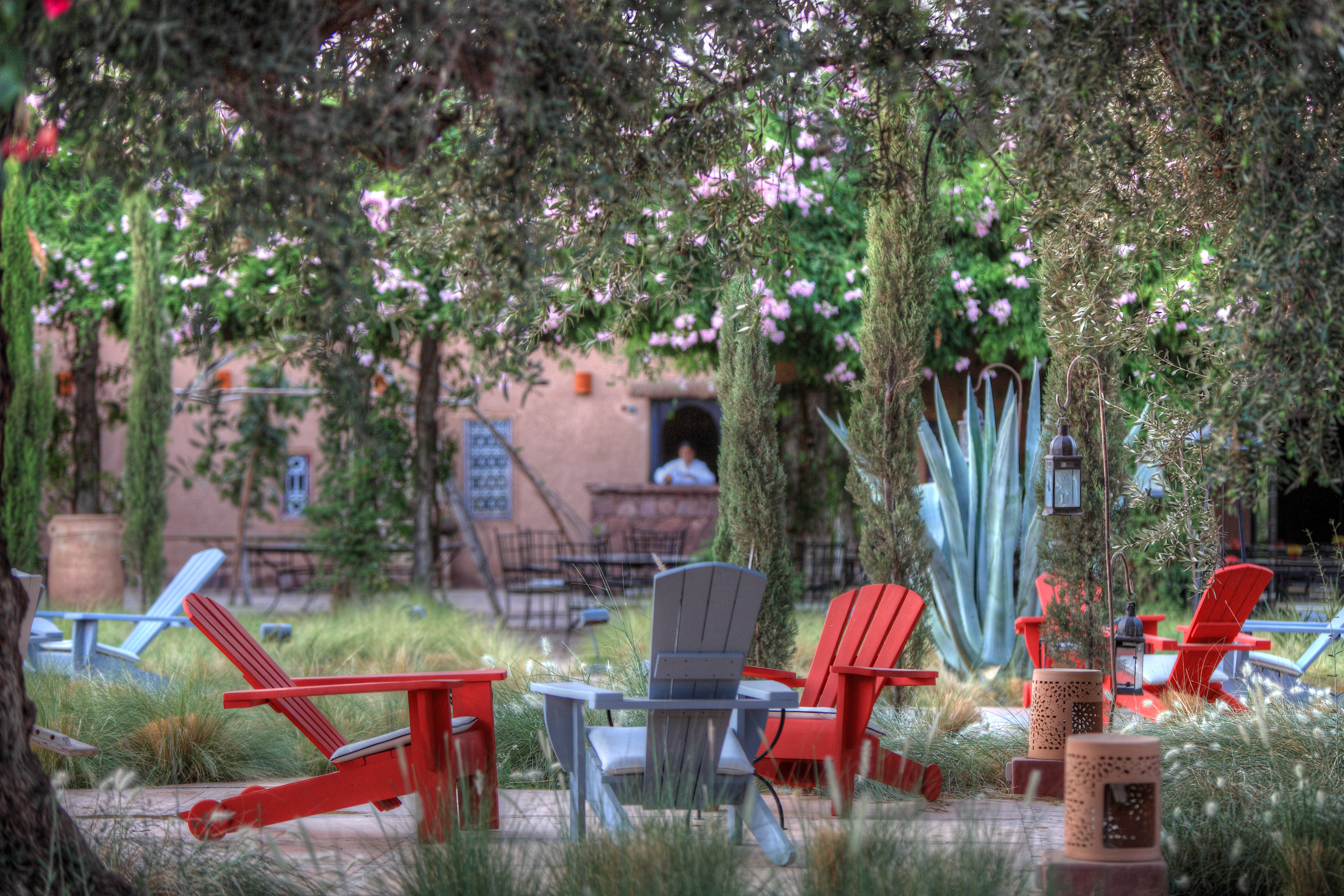Red Adirondack chairs in a tree-shaded courtyard at Beldi Country Club