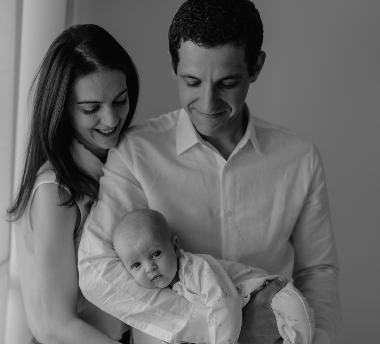 Amanda, Mohamed and baby Amira by a window, in black and white